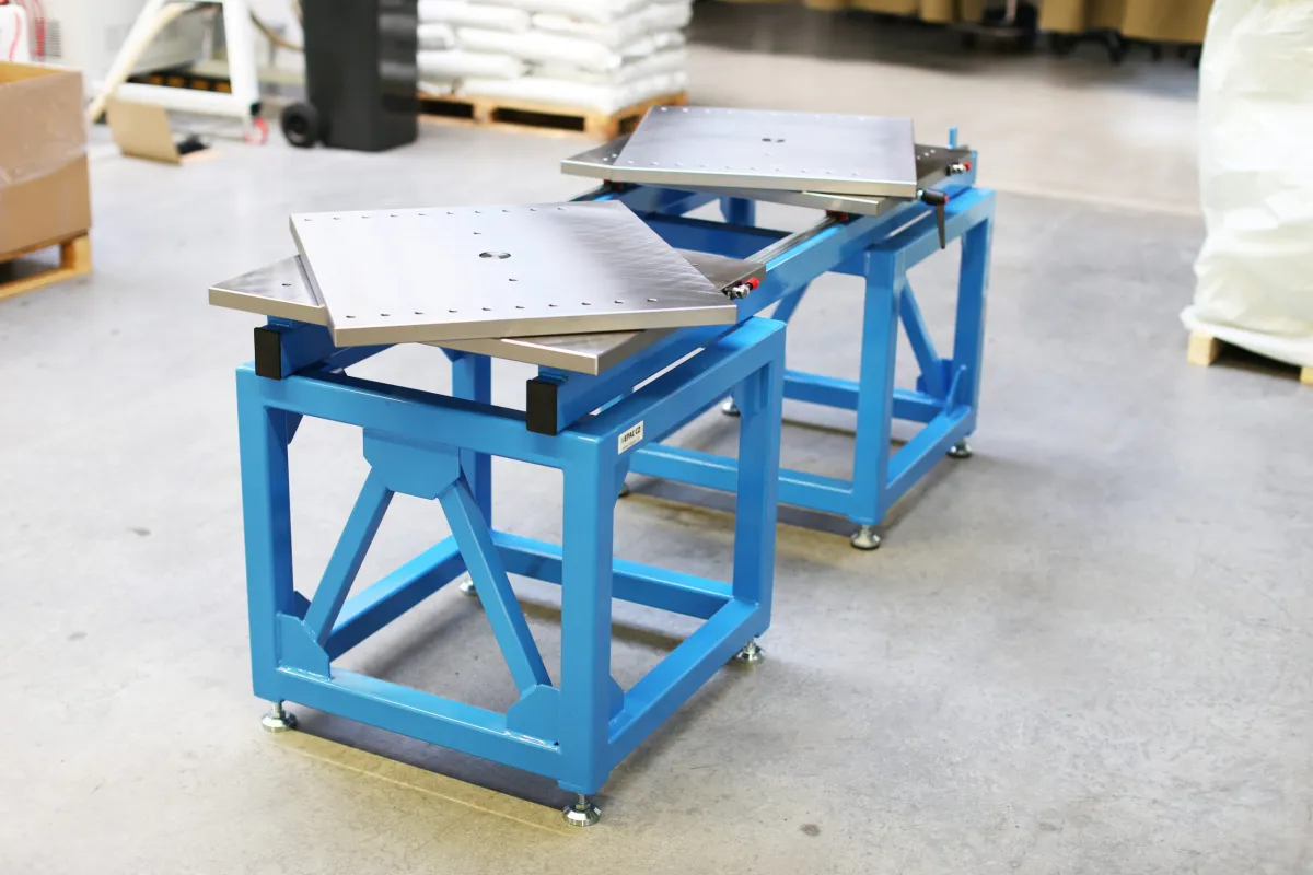 In der Werkhalle stehen zwei blaue Montagetische mit Metallplatten, an denen sich Werkzeuge bis 3 Tonnen öffnen, bewegen und bearbeiten lassen.