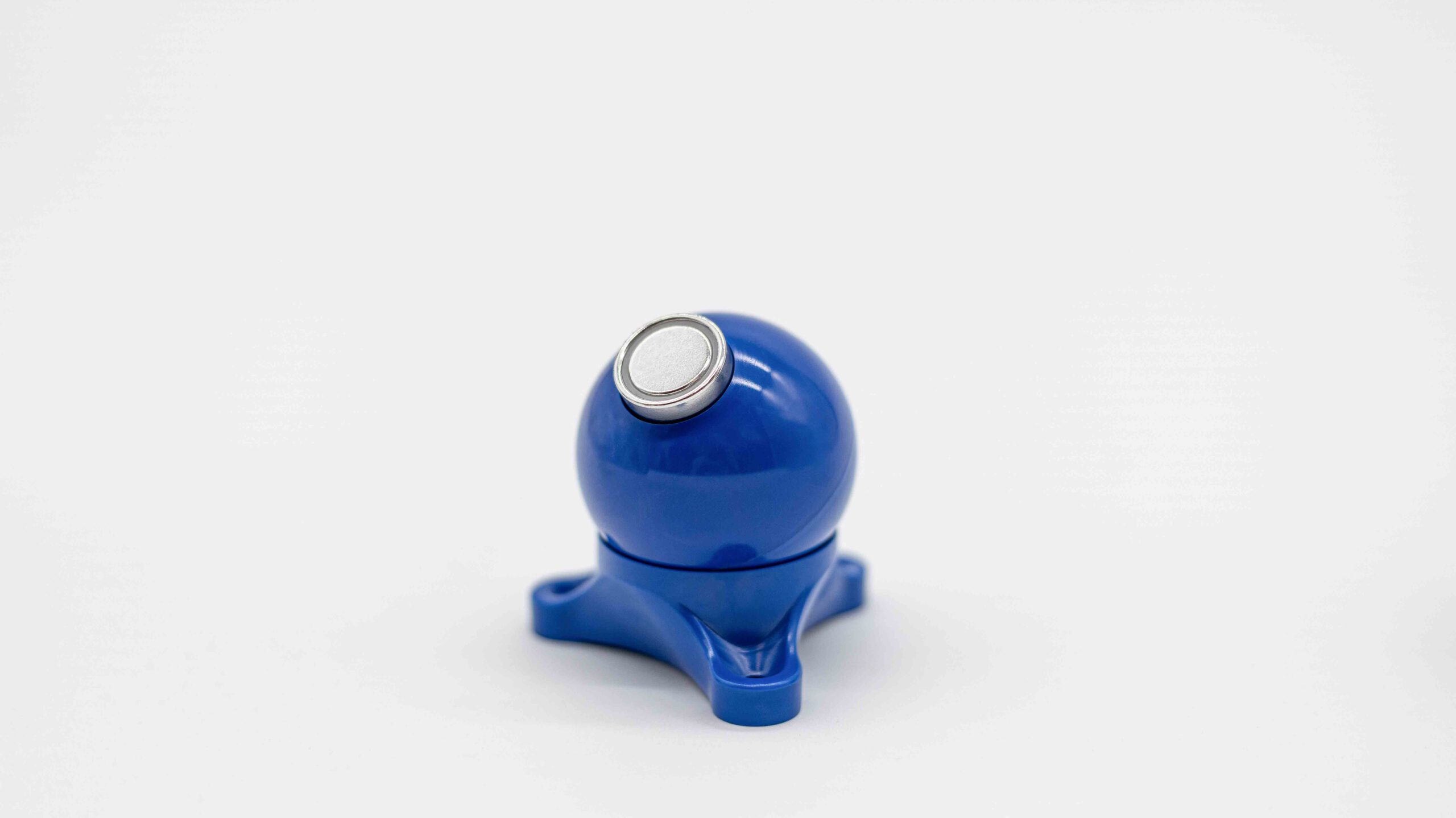 Der blaue MagBall mit glatter Rundform und silberner Metallkappe steht auf einer schlichten weißen Fläche und wirkt kompakt und modern.