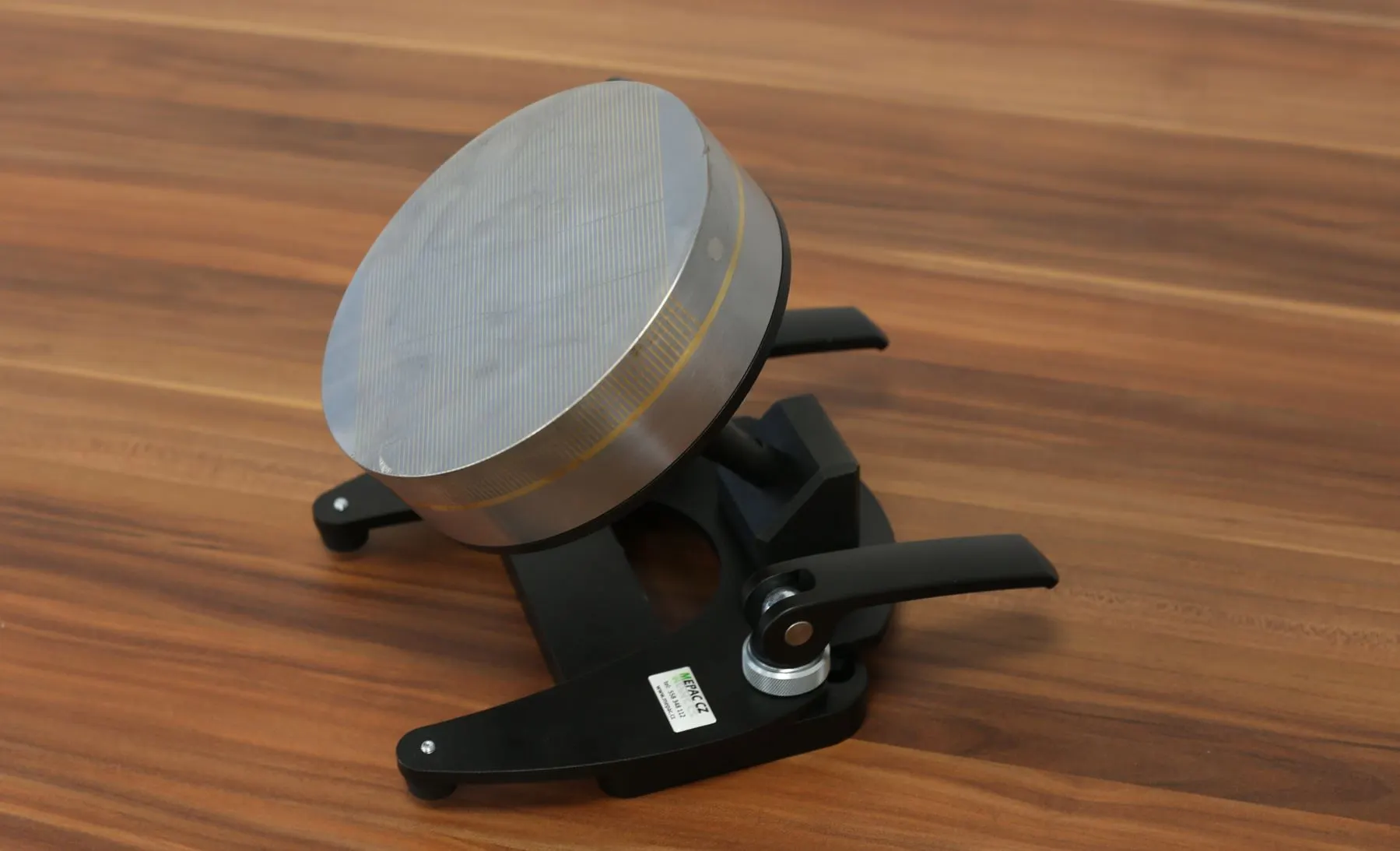 Eine runde Magnethalterung mit Spannklemmen hält ein schweres Metallwerkstück auf einer Holzoberfläche.