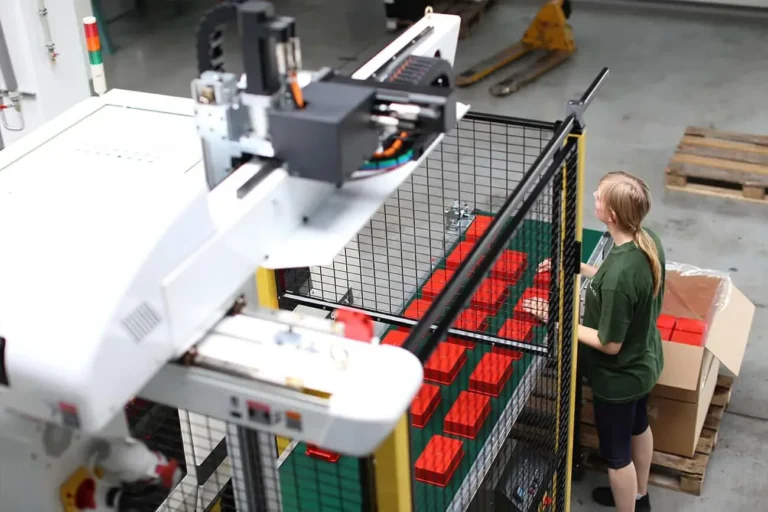 Handlingroboter entnimmt Spritzgussteile, Mitarbeiterin prüft und verpackt