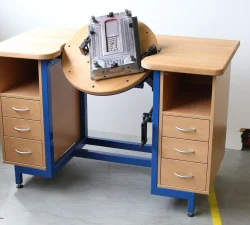 Eine Werkbank mit blauem Stahlgestell, Holzplatten und Schubladen trägt eine eingesetzte Spritzgussform auf der drehbaren Mittelplatte.