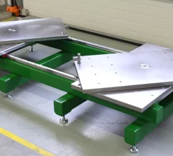 Ein grüner Werkzeugöffner KFM mit seitlich stehenden Ladeblättern trägt zwei silberne Formplatten in einer hellen Industriehalle auf Stellfüßen.