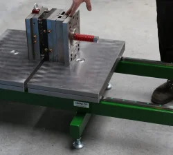 Ein kompakter Werkzeugöffner KFM hält eine Spritzgussform auf einer grün lackierten Konstruktion, während ein Bediener die Einheit einstellt.