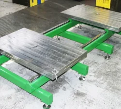 Der grüne Werkzeugöffner KFM steht mit zwei silbernen Auflageplatten leer auf dem Werkstattboden neben einer rutschfesten Fläche.