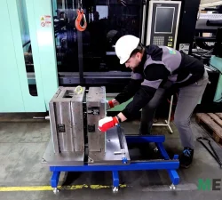 Ein Mitarbeiter in Schutzhelm und Handschuhen zieht an einer Spritzgussform auf dem mobilen Werkzeugöffner KFM von ToolyTech.