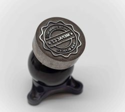 Ein gravierter Metallstempel mit Gravit-Logo steht auf einem dunklen Sockel vor hellem Hintergrund.