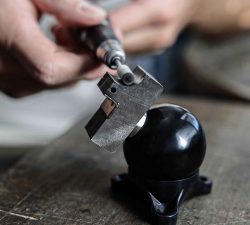 Ein Handwerkzeug bearbeitet eine schwarze Kugelhalterung auf einer Werkbank und erzeugt dabei präzisen Feinschliff.