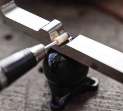 Ein metallisches Spannwerkzeug hält eine schwarze Kugel, während ein Schleifaufsatz dicht an der Verbindung arbeitet.