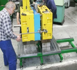 Ein älterer Mitarbeiter positioniert eine schwere Spritzgussform auf einem gelb-grünen Werkzeugöffner in einer Werkhalle für sichere Handhabung.