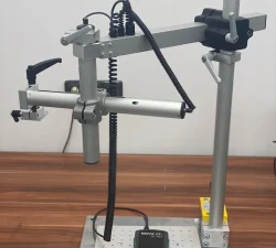 Ein mobiler Laserarm mit schwarzem Steuergerät steht auf einer perforierten Metallplatte auf einem Holztisch.