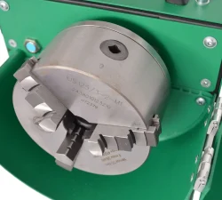 Ein vierbackiges Metallfutter mit Spannbacken sitzt in einer grünen Halterung und zeigt eine eingravierte Typenbezeichnung.