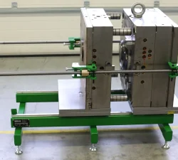 Ein mobiler Werkzeugöffner hält eine geöffnete Spritzgussform mit montierter Öffnungshilfe auf grünem Grundrahmen und Metallplatten in der Werkhalle.